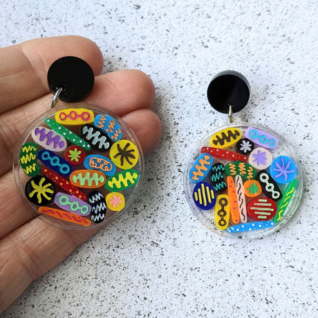 Petri Dish earrings Lots of little multicoloured acrylic 'microbes' sit inside an acrylic disc. Earrings hang from black toppers. 