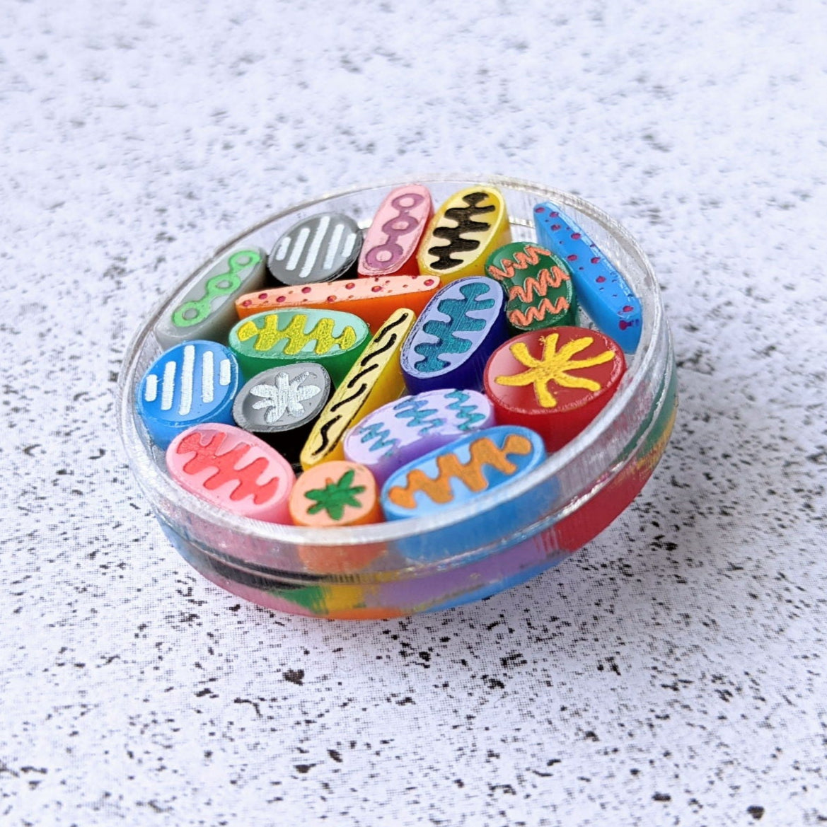 Petri Dish Brooch with tiny microbes. Laser cut in acrylic. Close up angled view.
