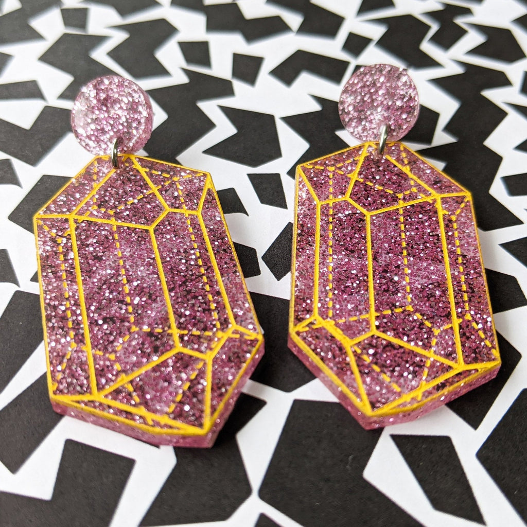 Pink glitter acrylic 'crysalline structure' earrings with yellow handpainted outlines of the crystal structure. Design 1.