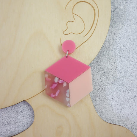 Laser cut acrylic statement cube earrings in pink colourway. Photo shows earrings being modelled. 