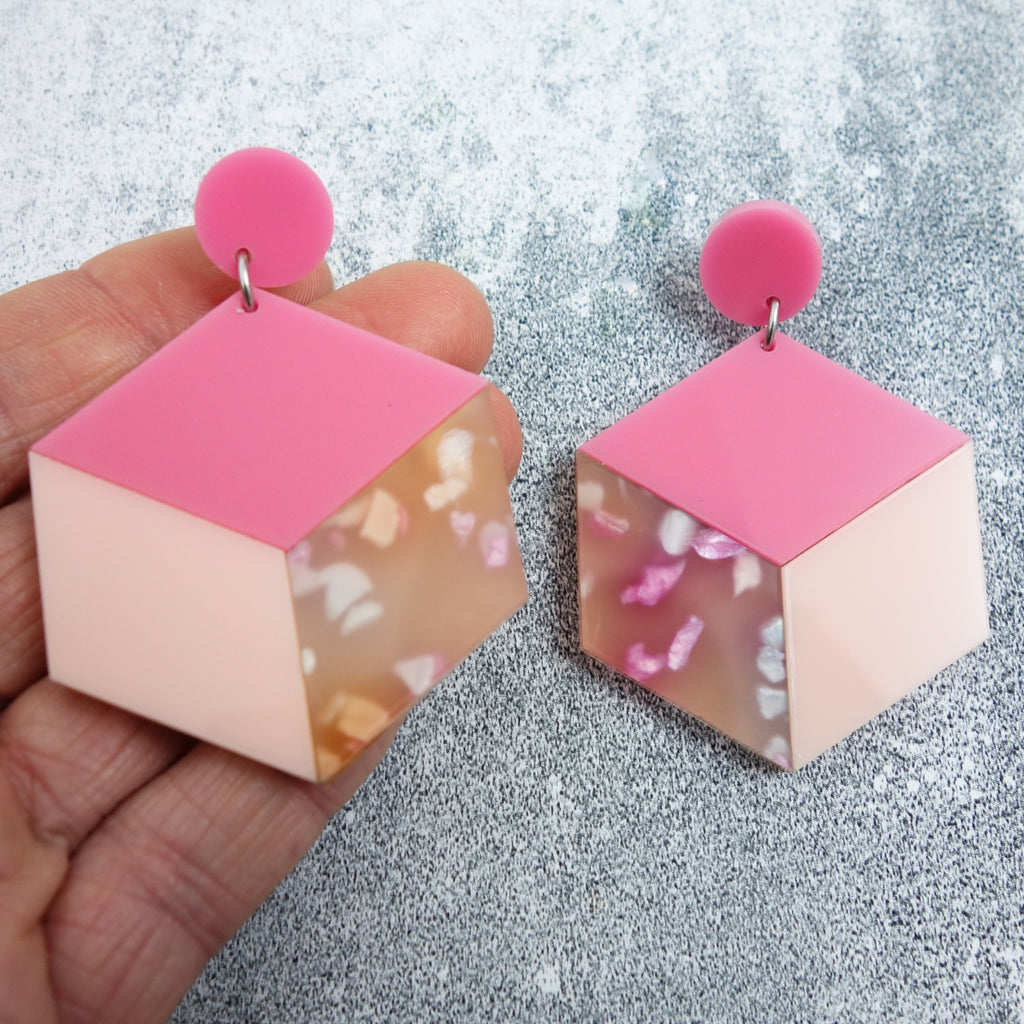 Laser cut acrylic statement cube earrings in pink colourway. Hand shown for scale.