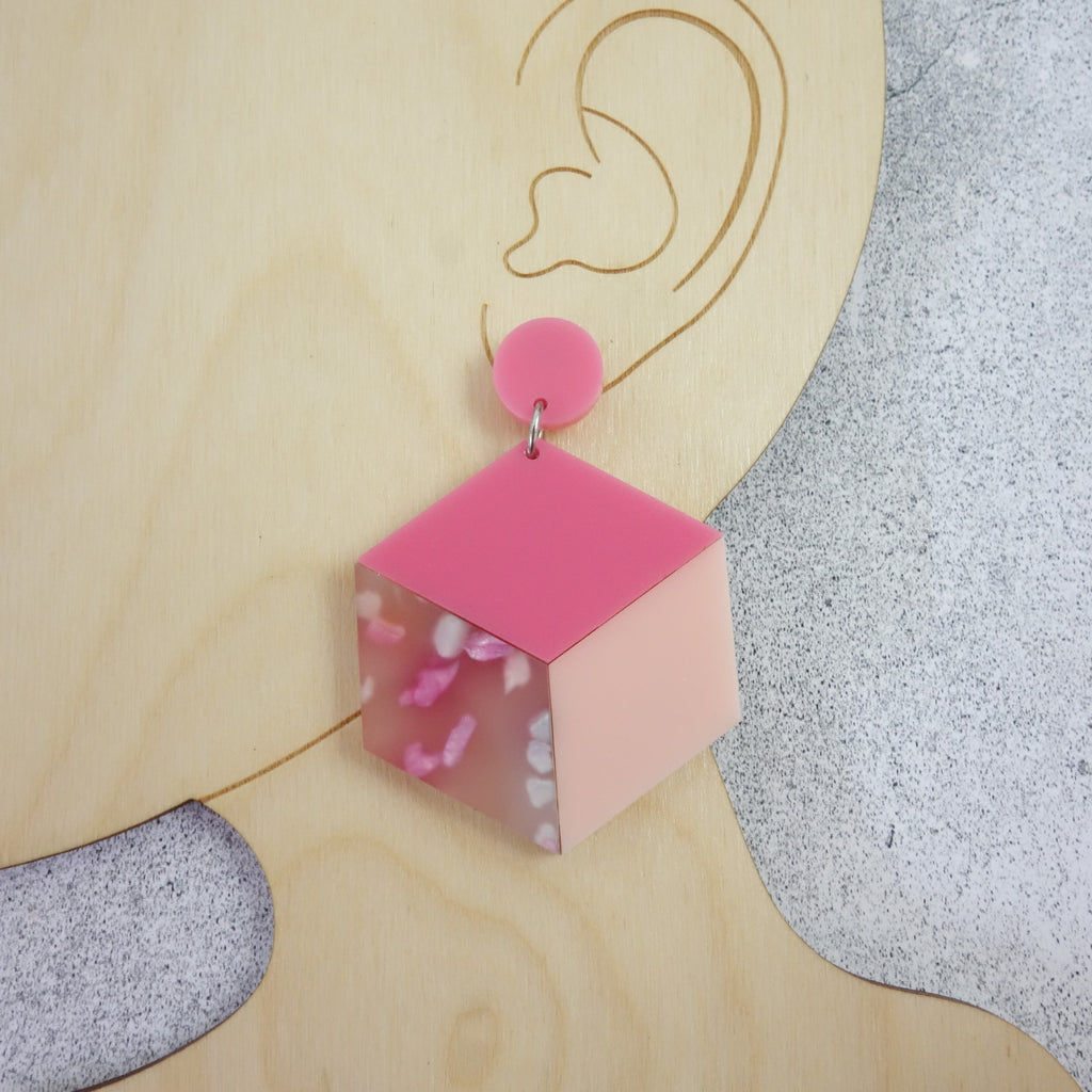 Laser cut acrylic statement cube earrings in pink colourway. Photo shows earrings being modelled. 
