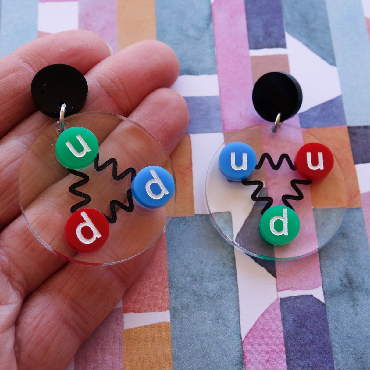 Laser cut acrylic quark earrings, , with green, red and blue up and down quarks, and hanging from black earring toppers.