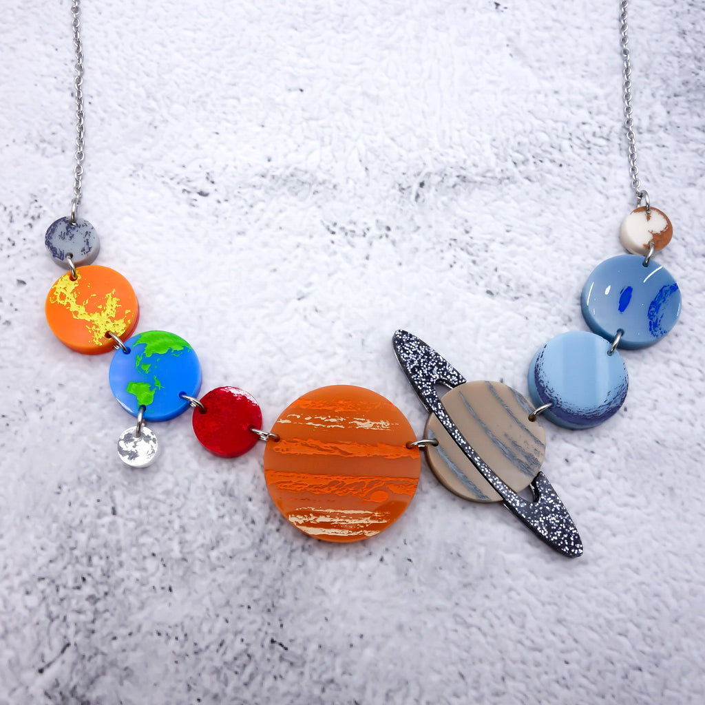 A solar system necklace, showing Mercury, Venus, Earth, the moon, Mars, Jupiter, Saturn, Uranus, Neptune and Pluto in differently coloured acrylics with handpainted highlights.