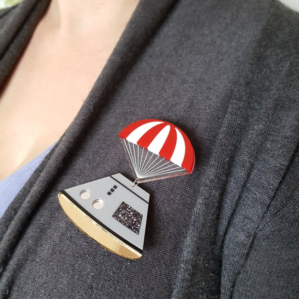 Space capsule brooch with red and white striped parachute, laser cut in acrylic. Modelled on cardigan.