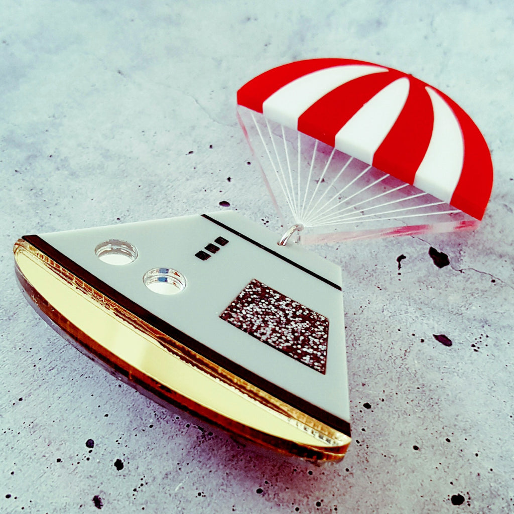 Space capsule brooch with red and white striped parachute, laser cut in acrylic. Side view.
