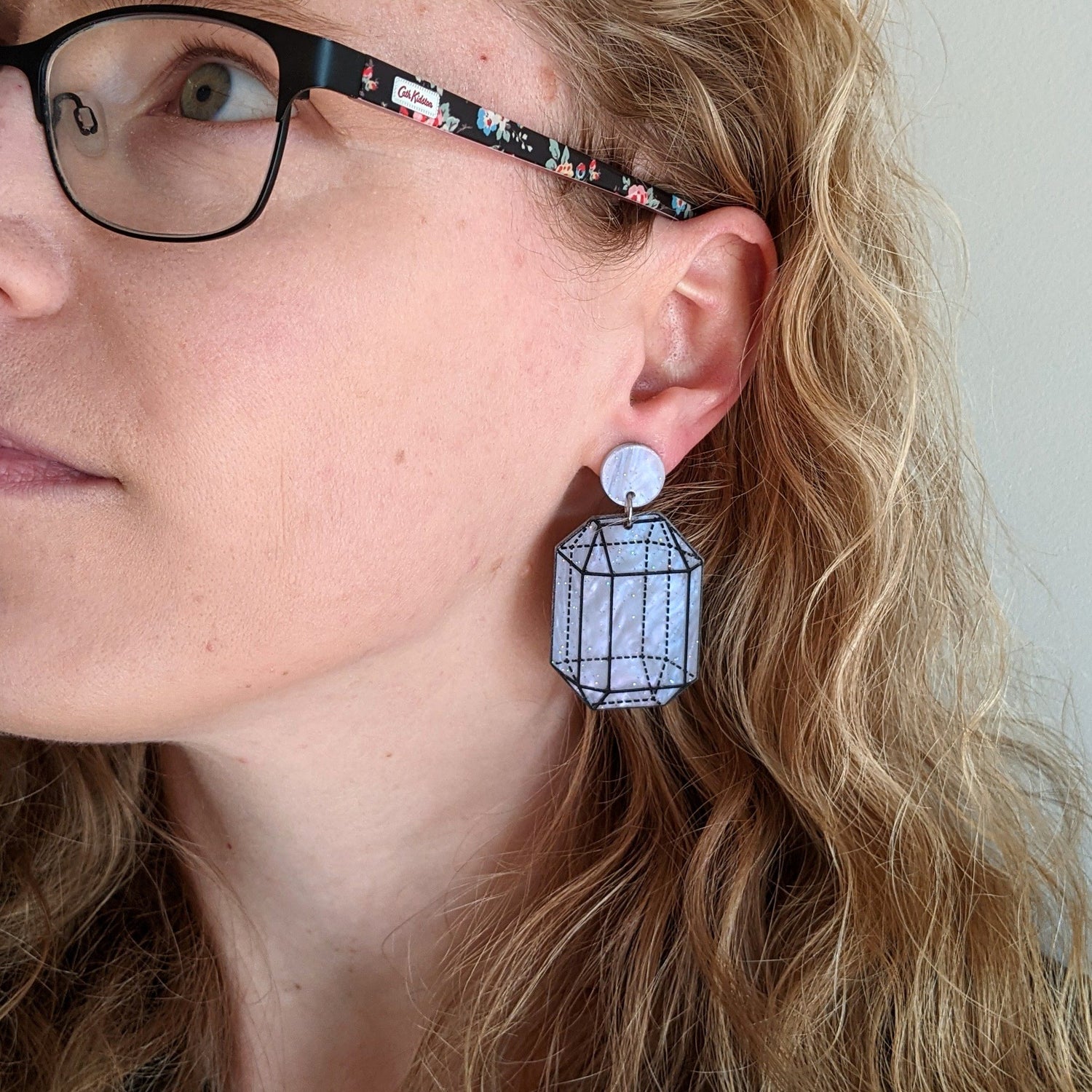 Glittery light blue and pink acrylic earrings with an etched crystalline design being modelled. 