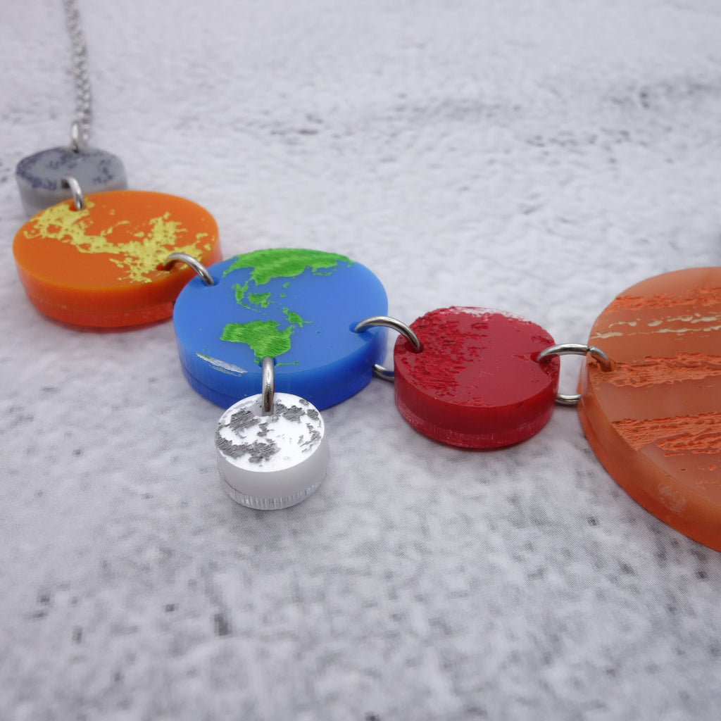 A  closeup view of a portion of a solar system necklace, showing Mercury, Venus, Earth, the moon, Mars and Jupiter in differently coloured acrylics with handpainted highlights. 
