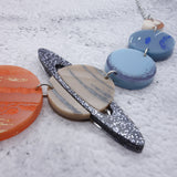 A  closeup view of a portion of a solar system necklace, showing Jupiter, Saturn, Uranus, Neptune and Pluto in differently coloured acrylics with handpainted highlights. 