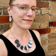 A woman modelling a laser cut acrylic moon phase necklace and moon phase earrings.