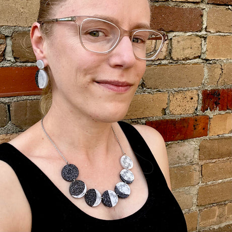 A woman modelling a laser cut acrylic moon phase necklace and moon phase earrings.