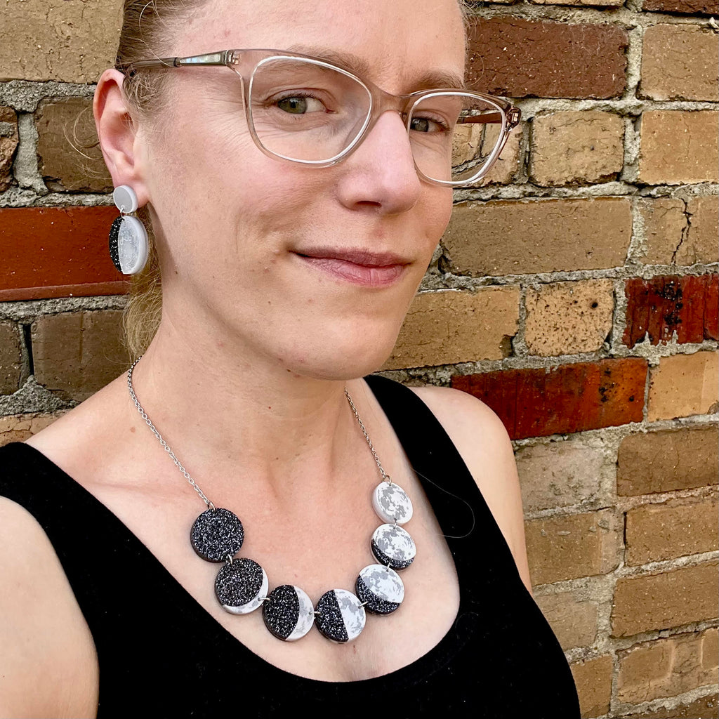 A woman modelling a laser cut acrylic moon phase necklace and moon phase earrings.