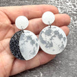 A pair of asymmetrical moon phase earrings, laser cut from pearlescent toned acrylic.