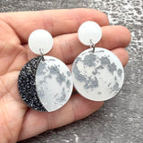 A pair of asymmetrical moon phase earrings, laser cut from pearlescent toned acrylic.