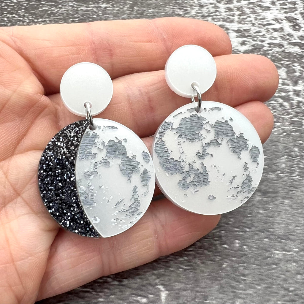 A pair of asymmetrical moon phase earrings, laser cut from pearlescent toned acrylic.